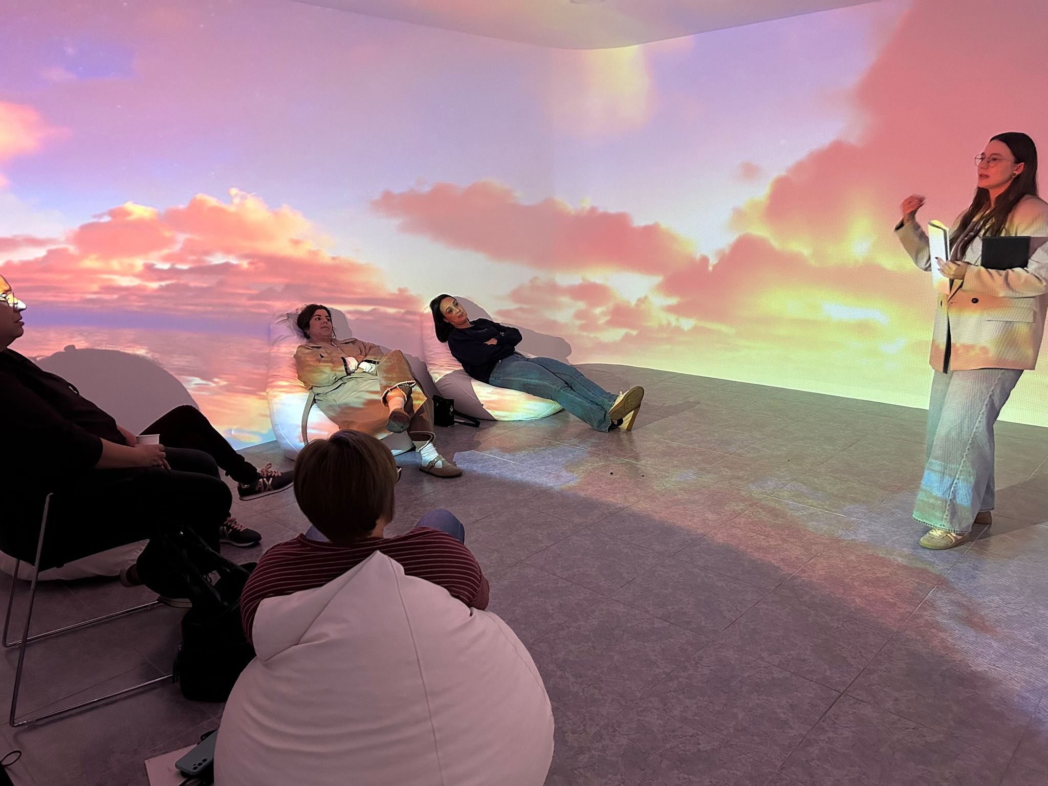 5 persones a una sala immersiva amb projecció de cel amb tons roses, groc i taronjes