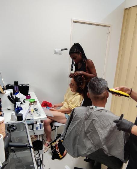 Un joven corta el cabello a un hombre y una chica hace trenzas africanas a una mujer
