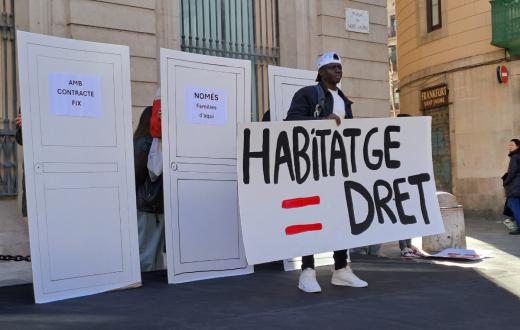 Una persona en situació de sensellarisme aixeca un cartell per demanar l'accés al dret de l'habitatge