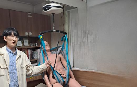 una persona coreana mostrant un robot per elevar una persona en un llit