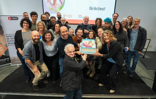 Personalitats de l'ajuntament, persones treballadores a Primera Llar, persones ateses i les seves veïnes agafen el pastís de celebració dels 10 anys