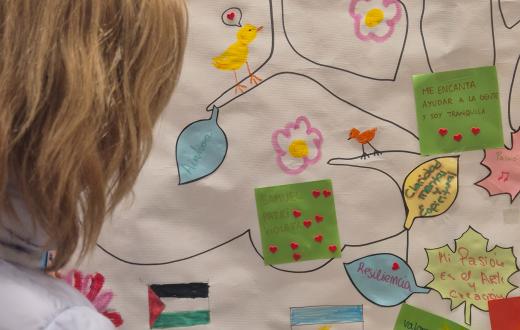 Una dona escriu en l'arbre simbòlic, que inclou amb arrels vinculades al lloc d’origen, un tronc amb valors i fortaleses i branques amb el nom 