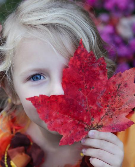A girl holding a tree leaf in front of her face