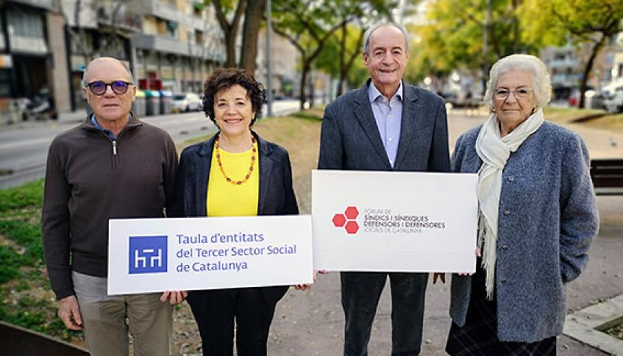 Two elderly couples displaying posters with the logos of the Taula and the Fòrum de Síndics i Síndiques