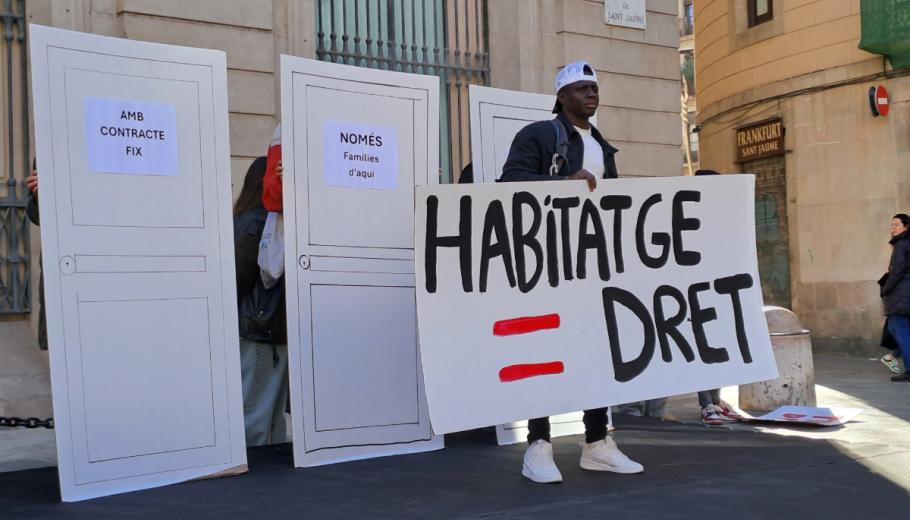 Una persona en situació de sensellarisme aixeca un cartell per demanar l'accés al dret de l'habitatge