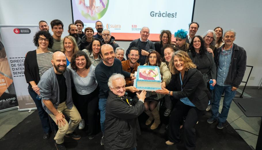 Personalitats de l'ajuntament, persones treballadores a Primera Llar, persones ateses i les seves veïnes agafen el pastís de celebració dels 10 anys