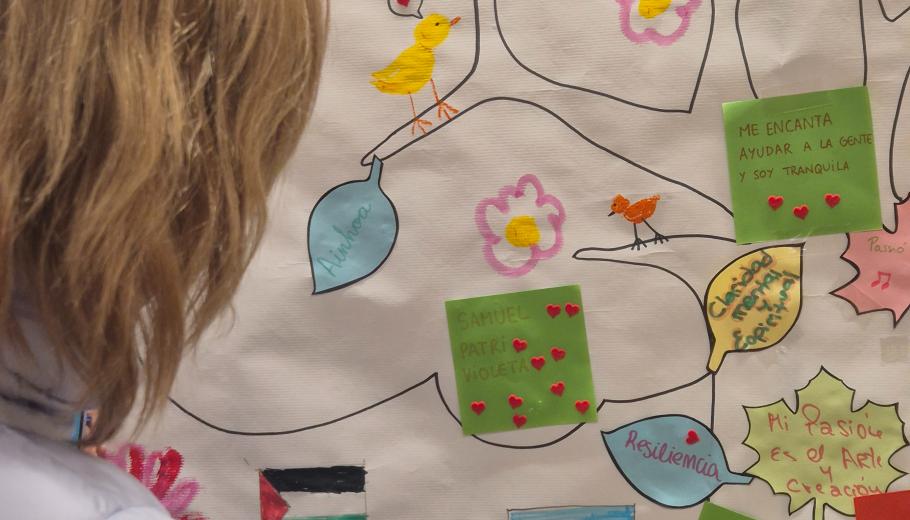 Una dona escriu en l'arbre simbòlic, que inclou amb arrels vinculades al lloc d’origen, un tronc amb valors i fortaleses i branques amb el nom 