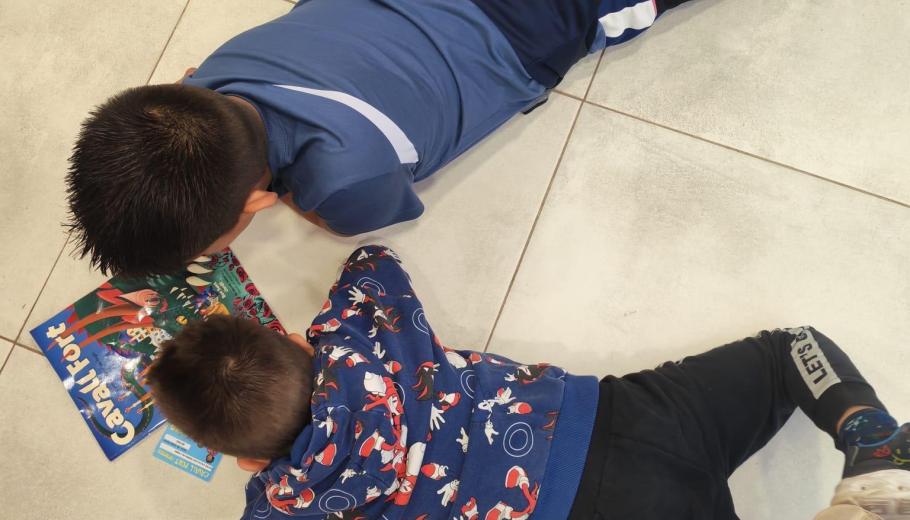 Dos nens del CA de Terres de l'Ebre estan estirats junts a terra llegint Cavall Fort