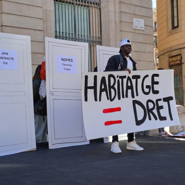 Una persona en situació de sensellarisme aixeca un cartell per demanar l'accés al dret de l'habitatge