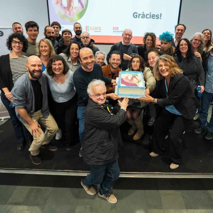 Personalitats de l'ajuntament, persones treballadores a Primera Llar, persones ateses i les seves veïnes agafen el pastís de celebració dels 10 anys