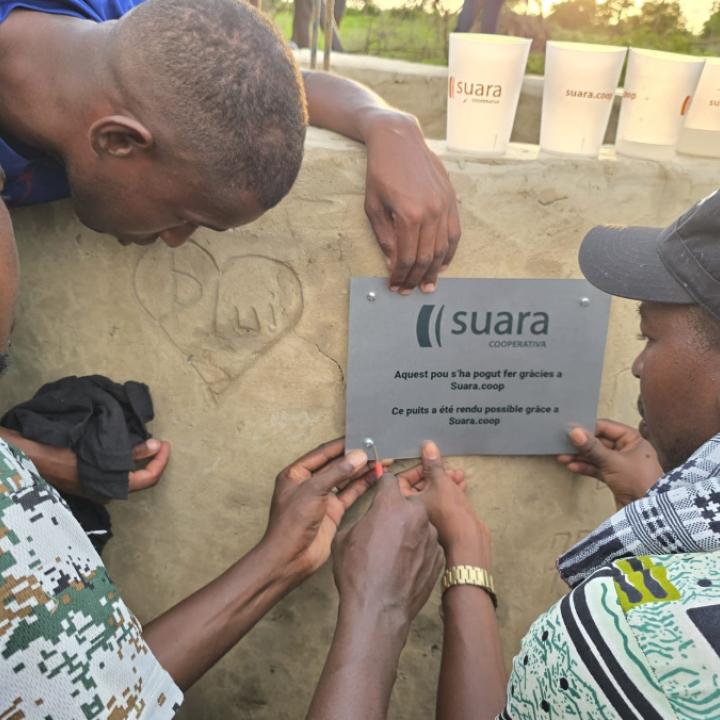Tres homes pengen la placa de Suara Cooperativa en el pou que s'ha construït al Senegal