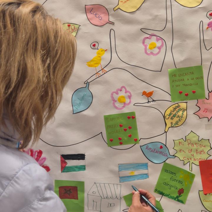 Una dona escriu en l'arbre simbòlic, que inclou amb arrels vinculades al lloc d’origen, un tronc amb valors i fortaleses i branques amb el nom 