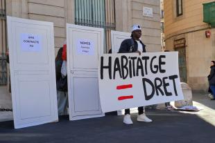 Una persona en situació de sensellarisme aixeca un cartell per demanar l'accés al dret de l'habitatge