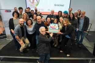 Personalitats de l'ajuntament, persones treballadores a Primera Llar, persones ateses i les seves veïnes agafen el pastís de celebració dels 10 anys