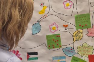 Una dona escriu en l'arbre simbòlic, que inclou amb arrels vinculades al lloc d’origen, un tronc amb valors i fortaleses i branques amb el nom 