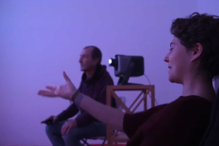 una noia senyalant a la mà i explicant la seva experiència al seu terapeuta en una sala de realitat immersiva
